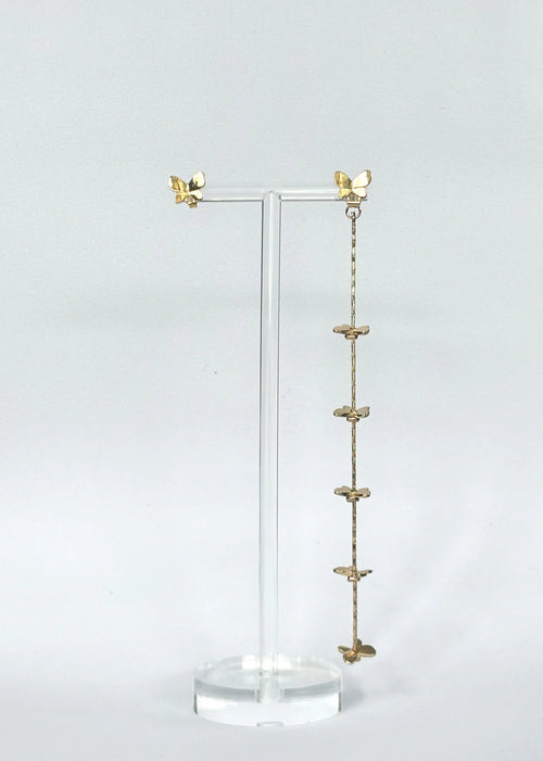 A gold butterfly drop earring displayed on a clear acrylic stand against a light gray background.
