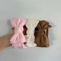 Three fabric bow hair clips in pink, cream, and brown, held in a hand against a plain light gray wall.