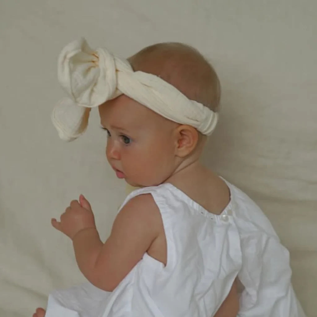 Baby wearing a white headband with a large bow against a plain background