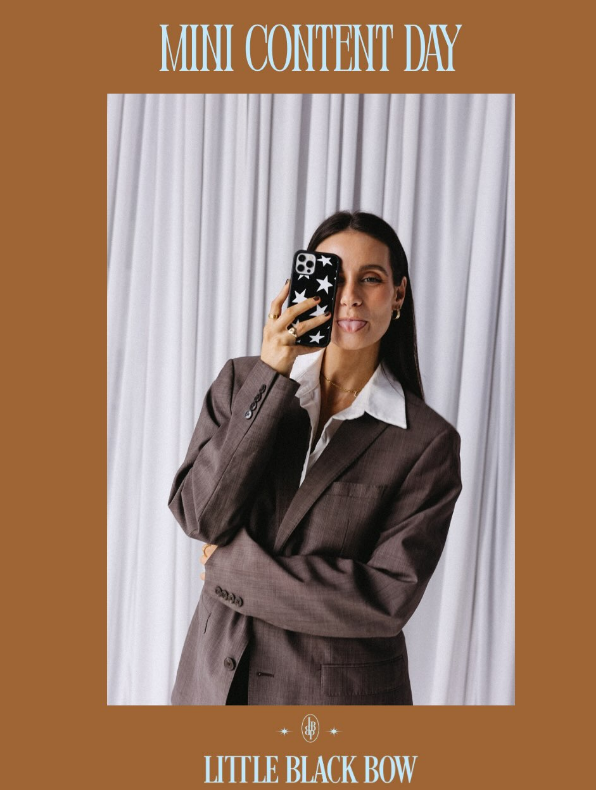 A woman takes a mirror selfie wearing a dark brown tailored blazer over a white collared shirt, holding a black patterned phone. The photo is framed within a tan graphic layout with the text 'MINI CONTENT DAY' at the top and 'LITTLE BLACK BOW' at the bottom.