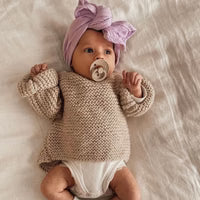 Baby wearing a knitted sweater and purple headband, lying on a soft surface.