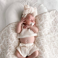 Newborn baby in white outfit with bow headband on floral blanket