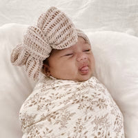 Newborn baby wearing a knitted hat and swaddled in a floral blanket on a white background