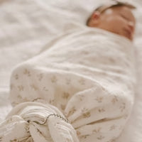 Baby wrapped in a soft, white blanket with a subtle pattern, lying on a neutral background.