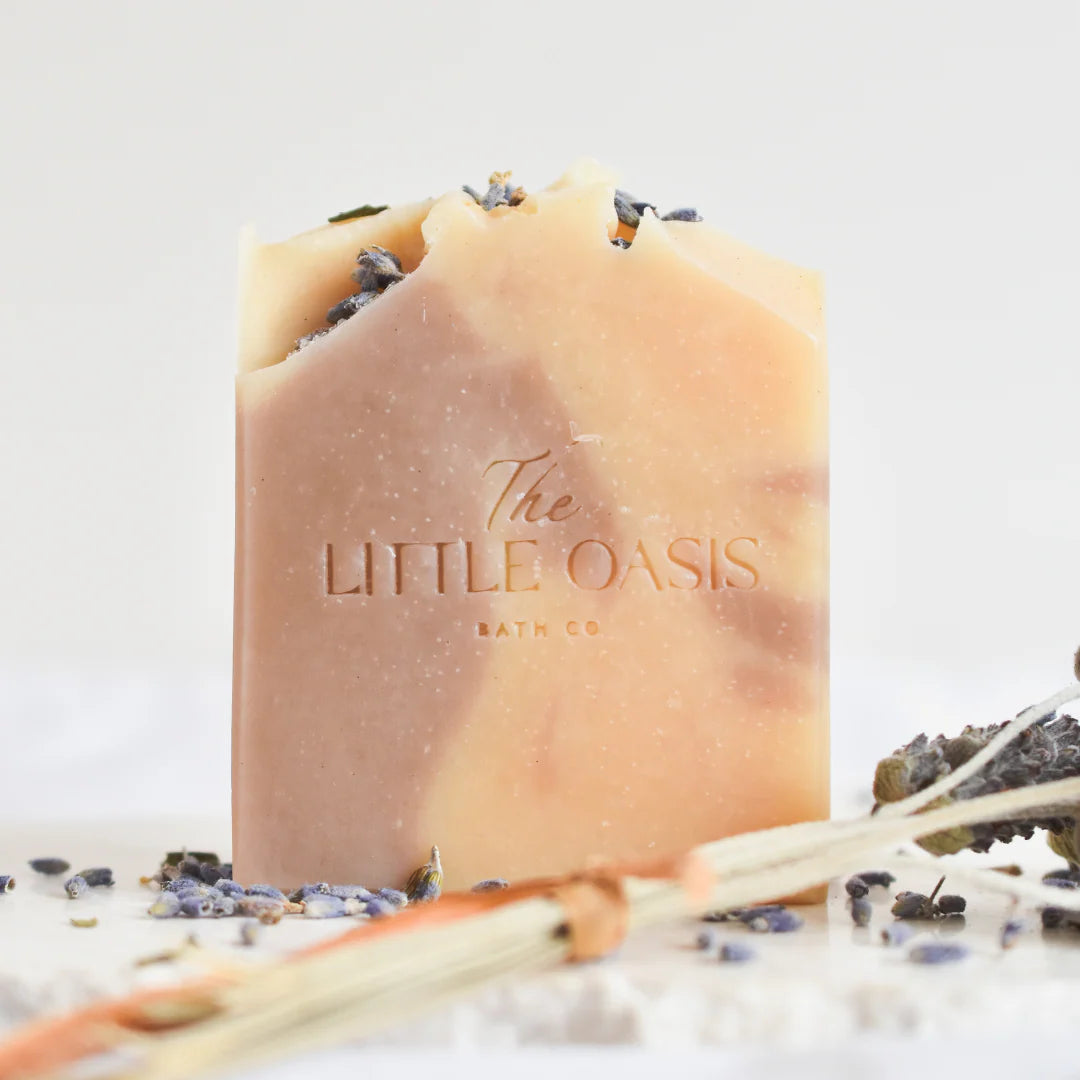 Bar of soap with 'The Little Oasis Bath Co' branding on a light background with lavender flowers.