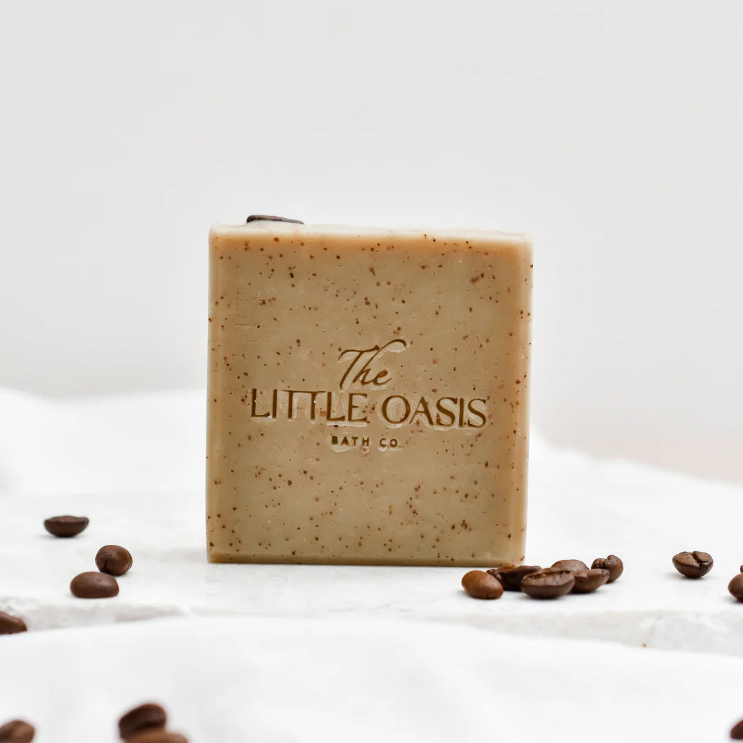 Bar of soap with 'The Little Oasis Bath Co' branding on a white background with coffee beans.